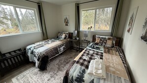 Una camera da letto con due letti, una finestra vista alberi, un termosifone e un piccolo tavolo con una lampada.