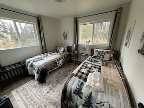 A bedroom with two beds, a window with a view of trees, a radiator, and a small table with a lamp. - 4 Bears-Quiet 1 acre Near Kenai River-Fish & Relax (Soldotna)