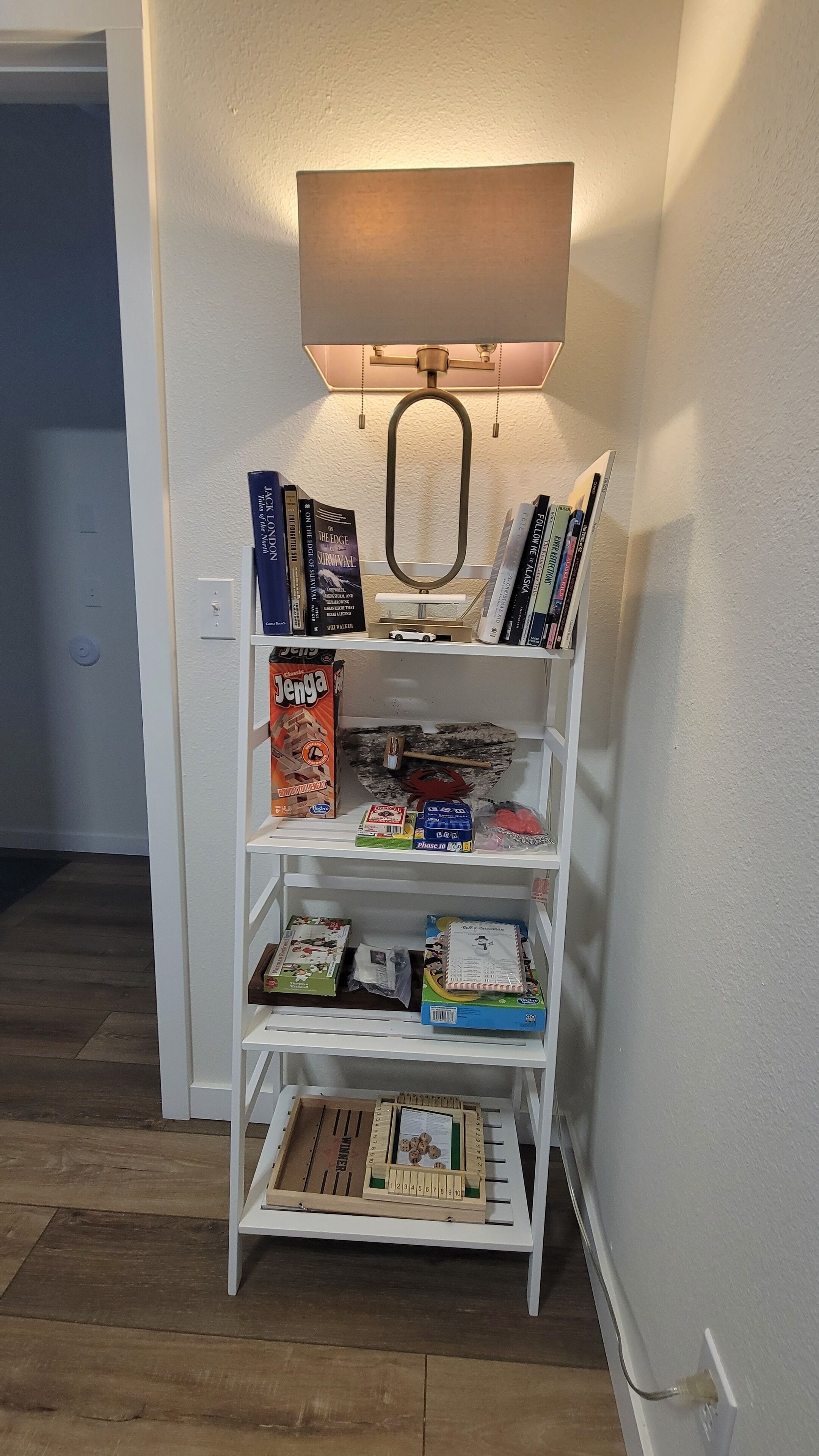Un estante blanco con libros, un juguete y un juego de mesa.