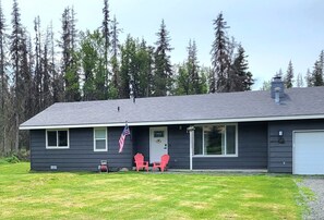 Ett envåningshus med en mörk fasad, en vit garageport och en veranda med två röda Adirondack-stolar. En amerikansk flagga är upphängd på verandan.