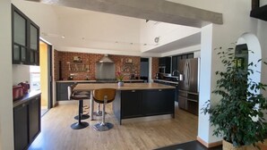 Une cuisine moderne dotée d’un grand îlot central, de meubles de rangement aux couleurs sombres et d’un mur d’accent en briques.