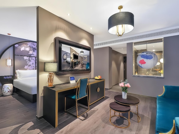 Habitación de hotel con cama, escritorio, silla, mesas redondas, televisión y un espejo grande.