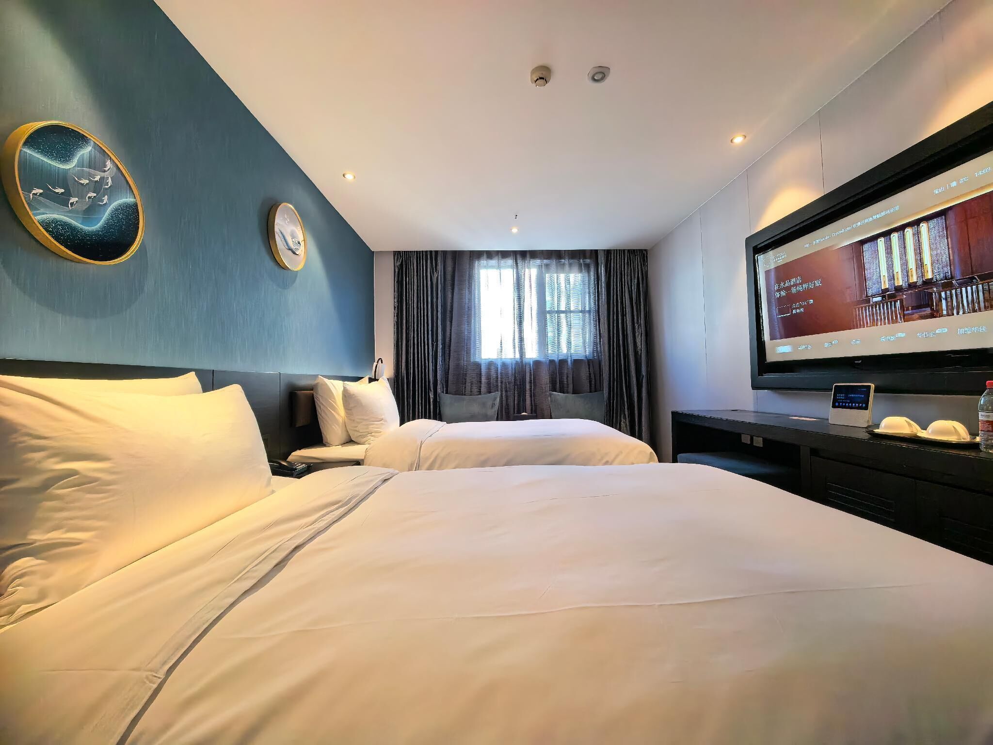 Une chambre d’hôtel avec deux lits, une télévision, une horloge et une fenêtre avec des rideaux.