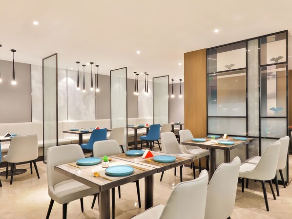 Un comedor moderno con varias mesas y sillas, que presenta un diseño minimalista con líneas depuradas y una paleta de colores neutros.