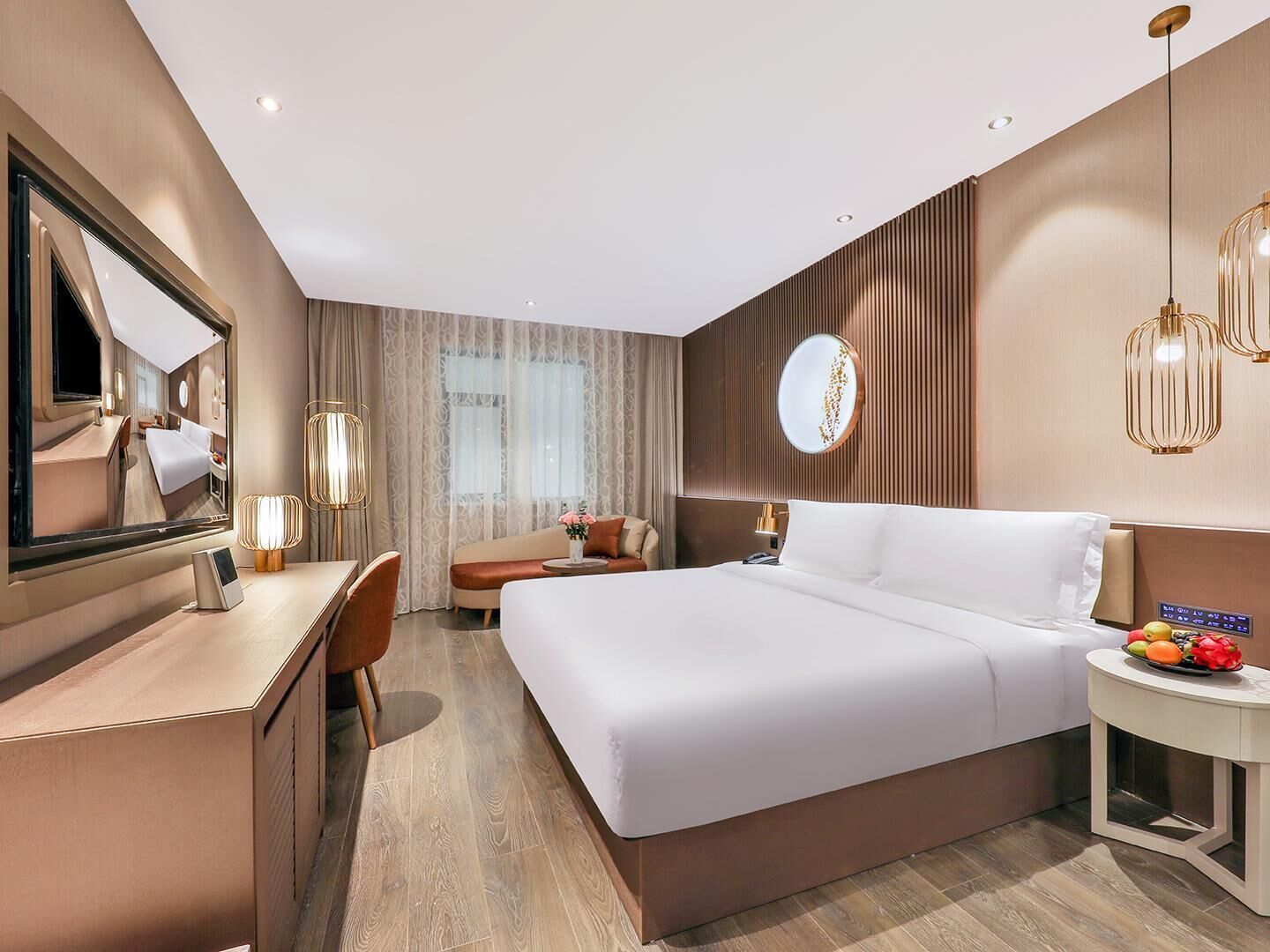 Habitación de hotel moderna con una cama grande, un escritorio, una silla, un espejo redondo y una mesita de noche con fruta.