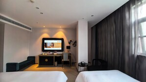 Una habitación de hotel con dos camas, un escritorio con computadora, un televisor montado en la pared y una ventana con cortinas.