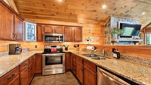 Une cuisine dotée de meubles en bois, d’appareils électroménagers en acier inoxydable, de plans de travail en granit et d’une cheminée en pierre.
