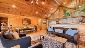 L’intérieur d’un chalet confortable, avec des murs en rondins, une table à manger en bois, un canapé et une table basse.