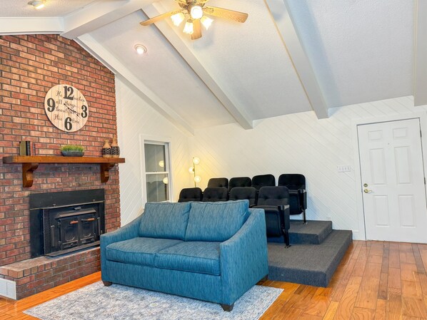 A cozy living room with a brick fireplace, a blue sofa, and a ceiling fan.