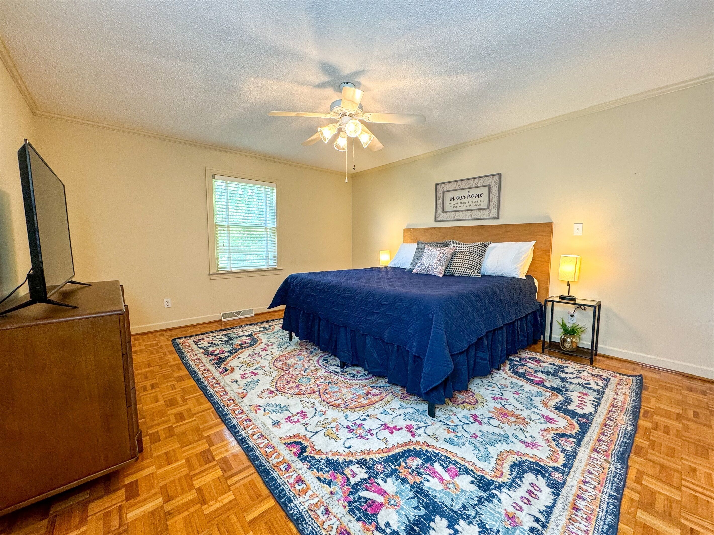A bedroom with a bed, a ceiling fan, a window, a nightstand, and a television.