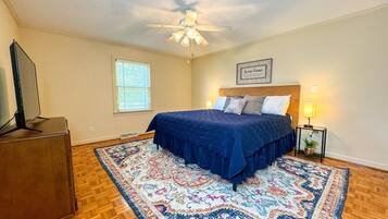 A bedroom with a bed, a ceiling fan, a window, a nightstand, and a television.