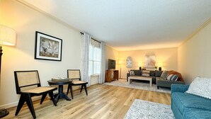 A living room with a wooden floor, a sofa, a coffee table, a TV, and a dining area with chairs and a table. - HUGE Theater Room~ Private Farm Stay- Sleeps 10 (Rome)