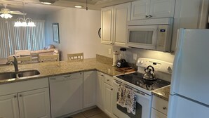 A modern kitchen with white cabinets, a built-in microwave, a stove, and a refrigerator. - Waterfront Snowbird retreat with screened-in lanai and heated pool! (Cape Coral)