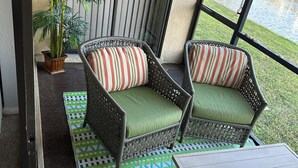 A balcony with wicker chairs, a small table, and a potted plant. - Waterfront Snowbird retreat with screened-in lanai and heated pool! (Cape Coral)