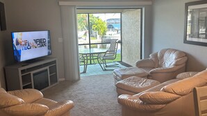A living room with a television, a sofa, and a dining table with chairs. - Waterfront Snowbird retreat with screened-in lanai and heated pool! (Cape Coral)