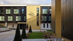 Un edificio moderno con área de recepción, jardín cuidadosamente ajardinado y un logotipo en la fachada.