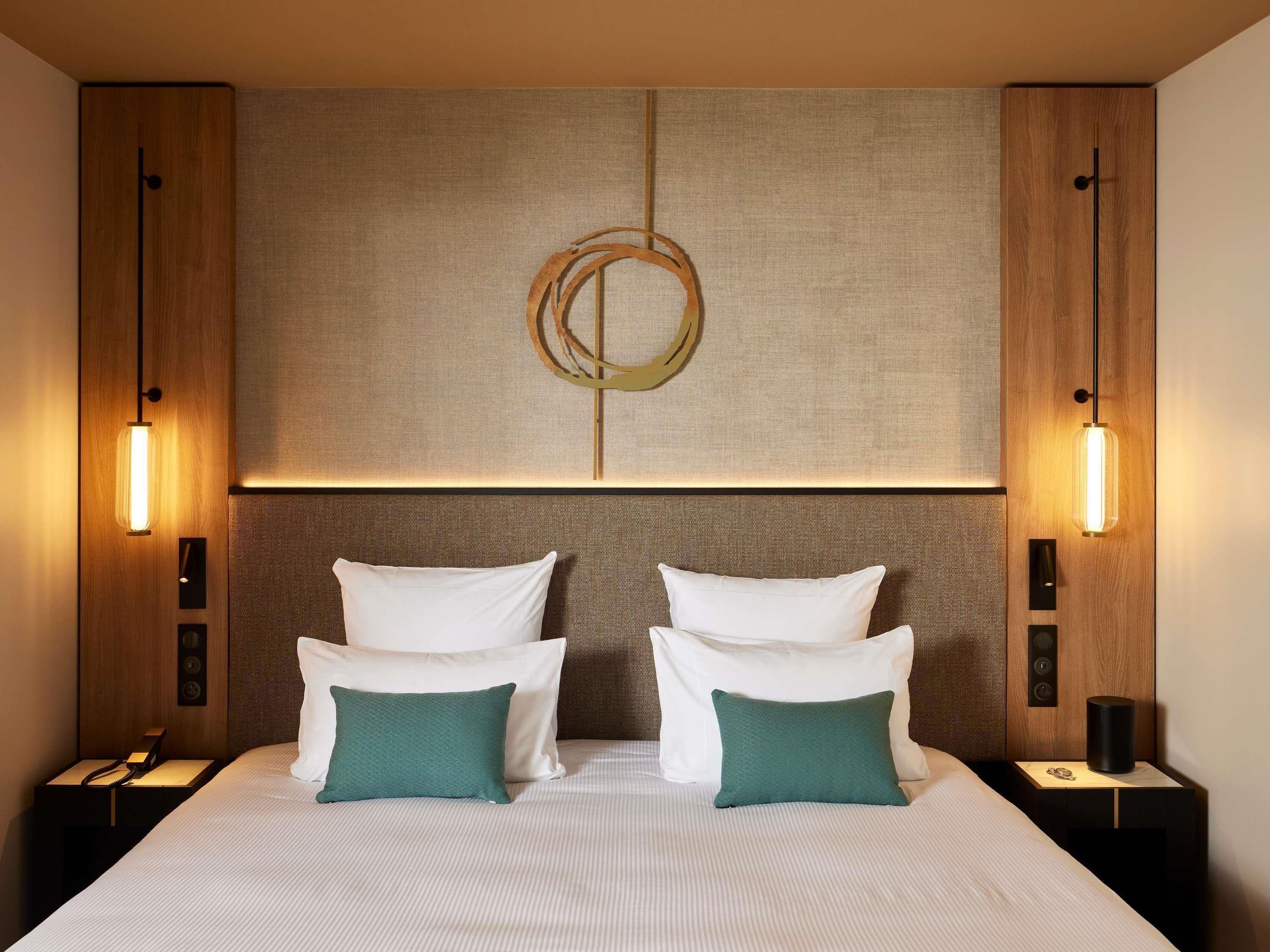 Hotelkamer met een groot bed, twee nachtkastjes, een wandlamp en een gestructureerd wandpaneel.