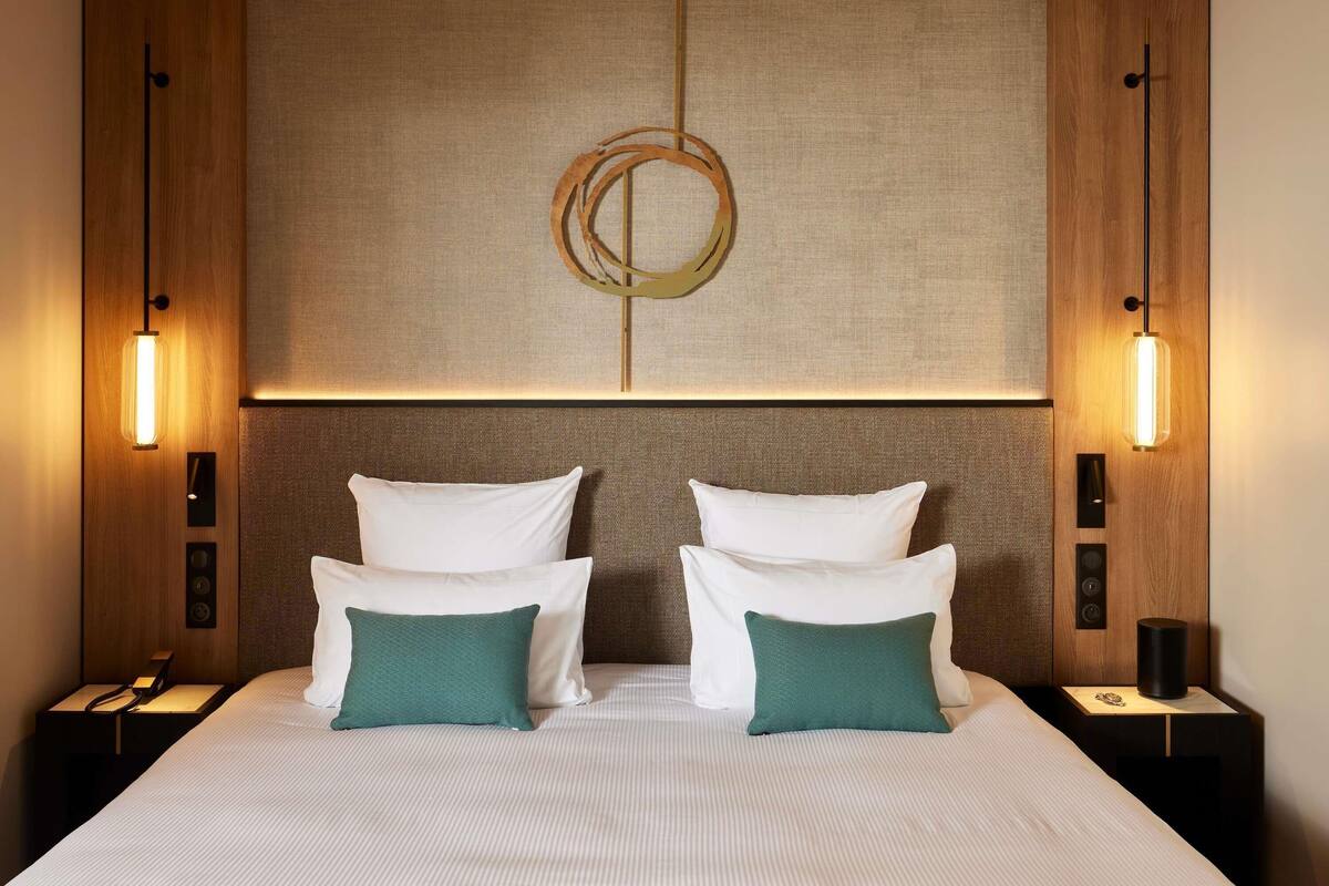 Ein Hotelzimmer mit einem großen Bett, zwei Nachttischen, einer Wandleuchte und einer Wandpaneele mit Struktur.