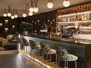 A bar area with a long counter, multiple stools, and a variety of bottles. - Domaine du Liziec Vannes - MGallery Collection (Vannes)