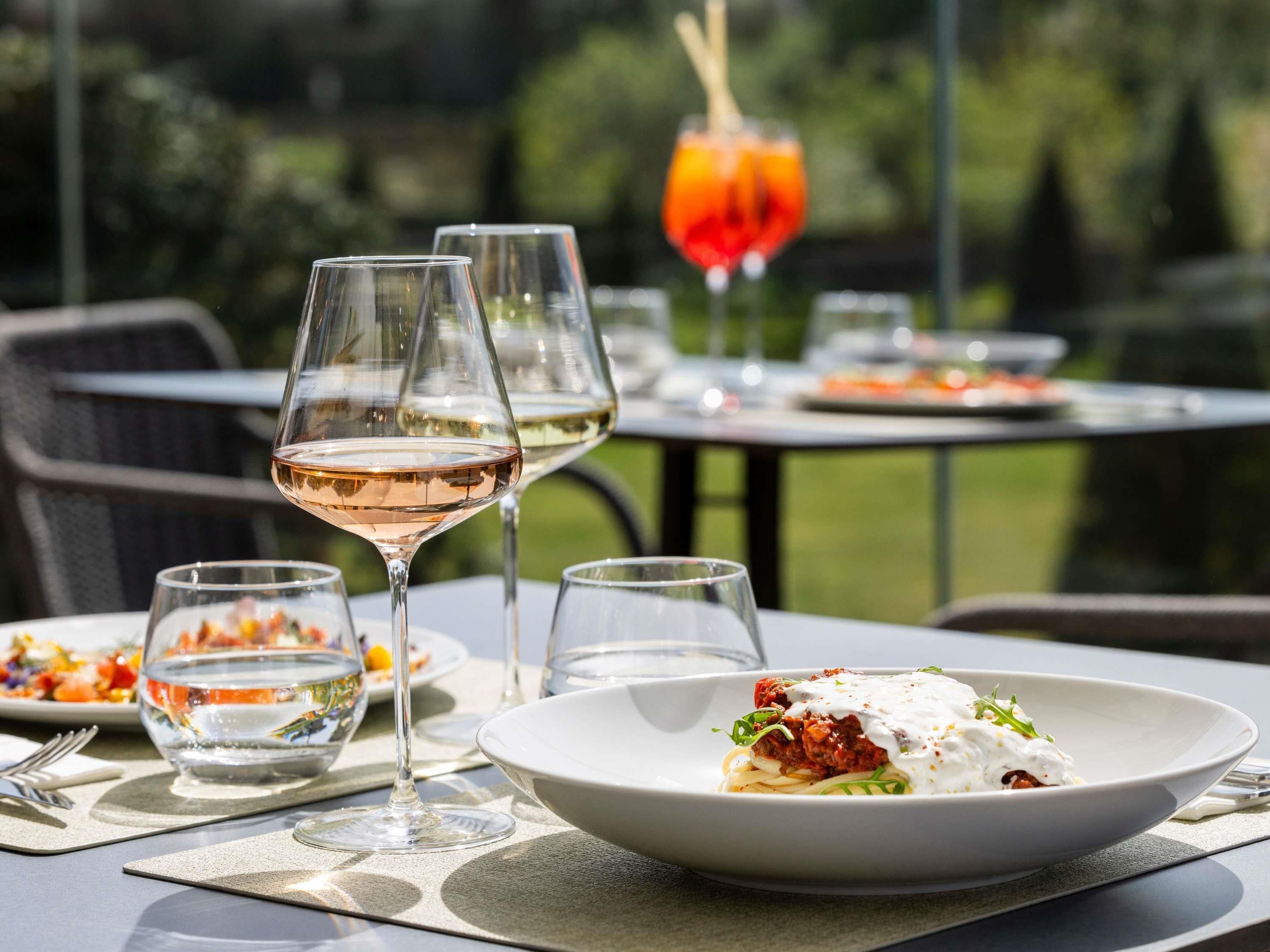 A dining table with a plate of pasta, two wine glasses, and a glass of water.