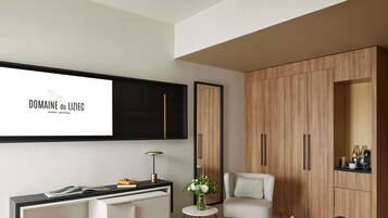 A modern living room with a sofa, a small table with a vase, a chair, a TV mounted on the wall, and a wooden wardrobe.