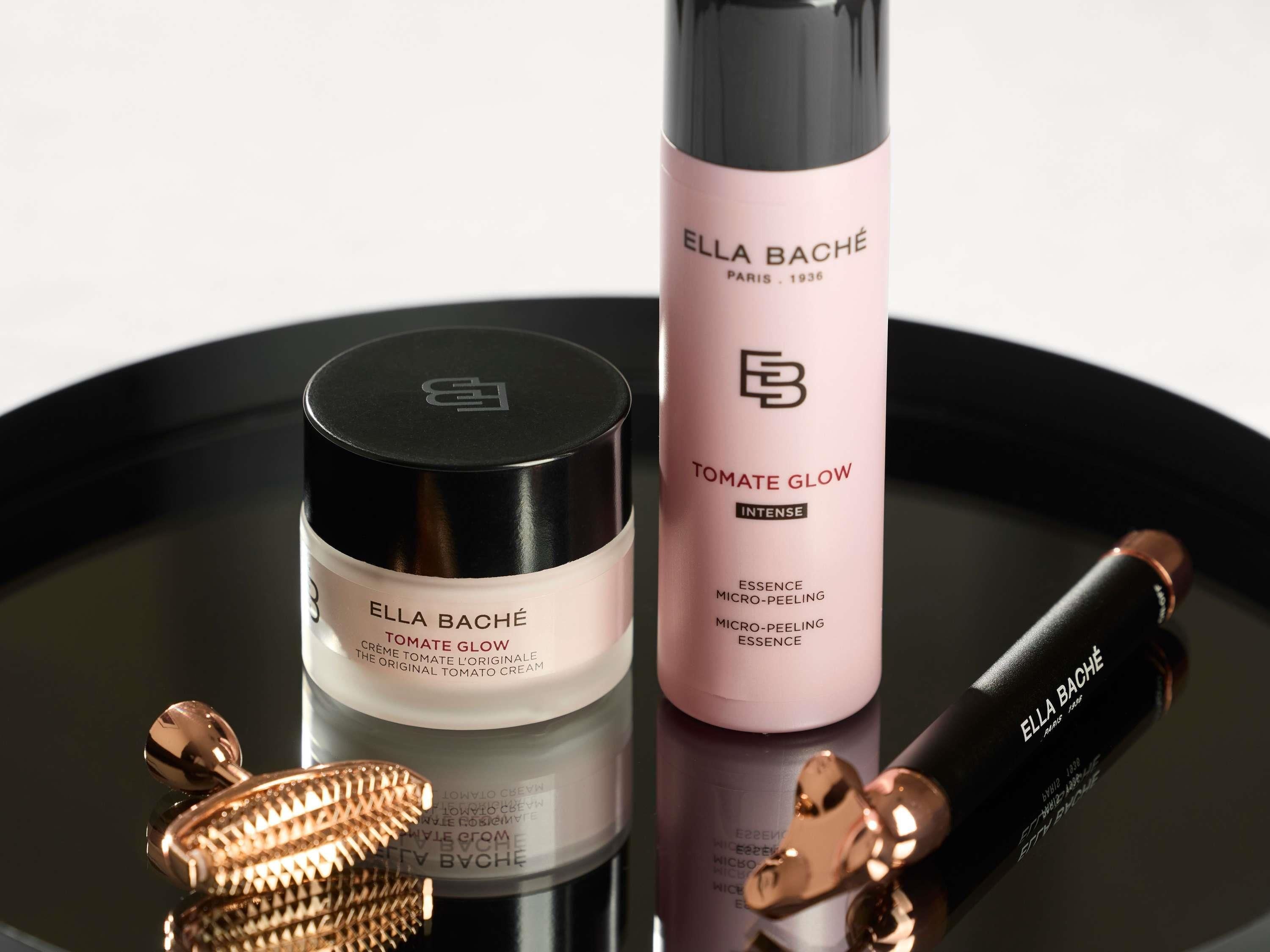 Trois contenants de produits cosmétiques de la marque « ELLA BACHÉ » et du produit « TOMATE GLOW », placés sur une surface réfléchissante.