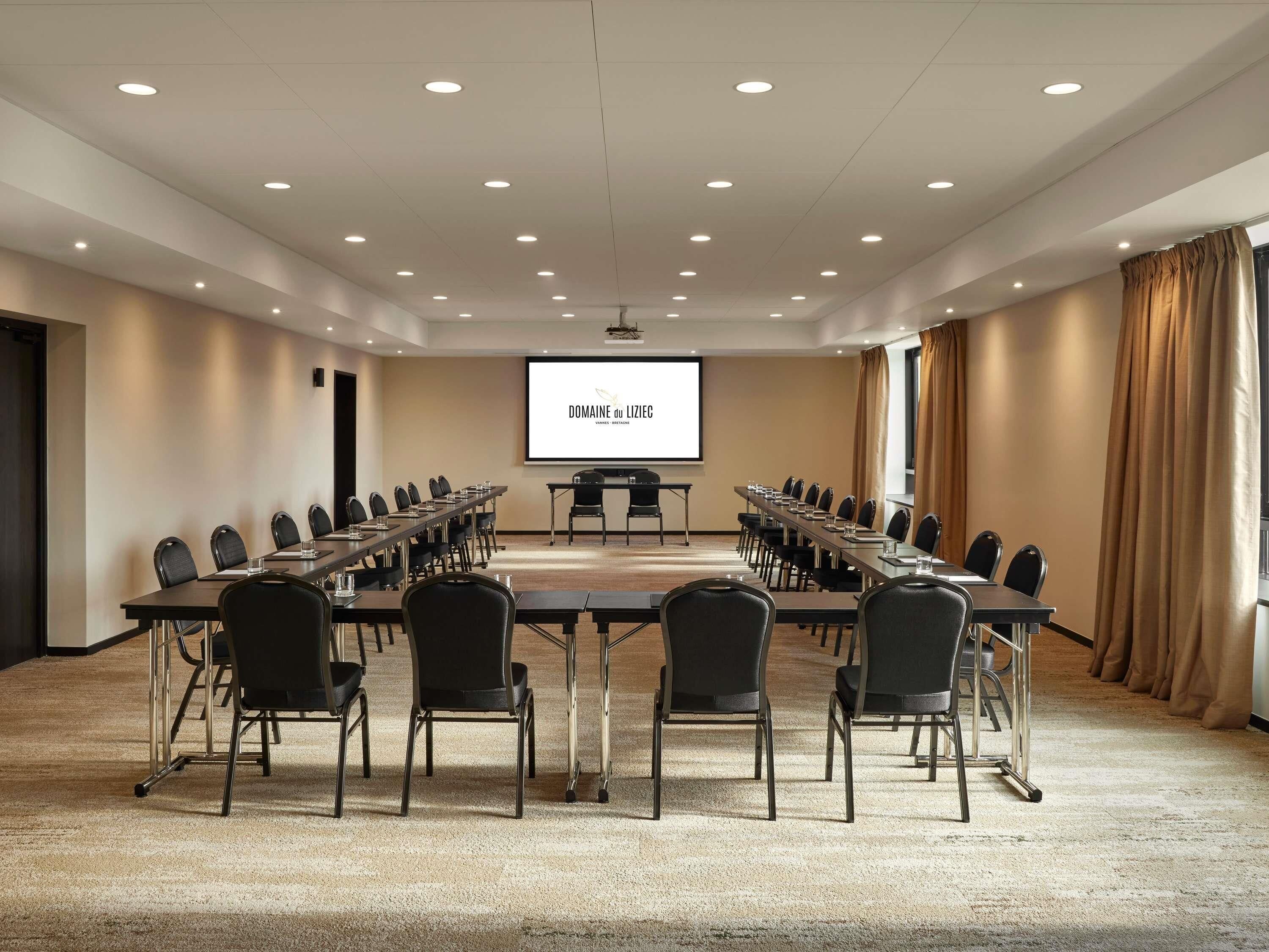 Une salle de conférence avec une longue table, des chaises, un écran de projection et un sol recouvert de moquette.