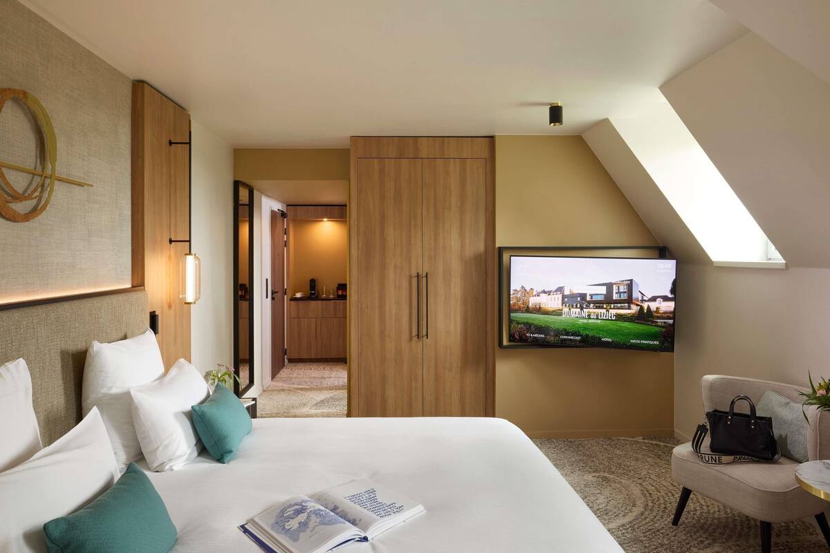Ein Hotelzimmer mit Bett, Fernseher, Schreibtisch und Blick auf das Hotelgebäude.