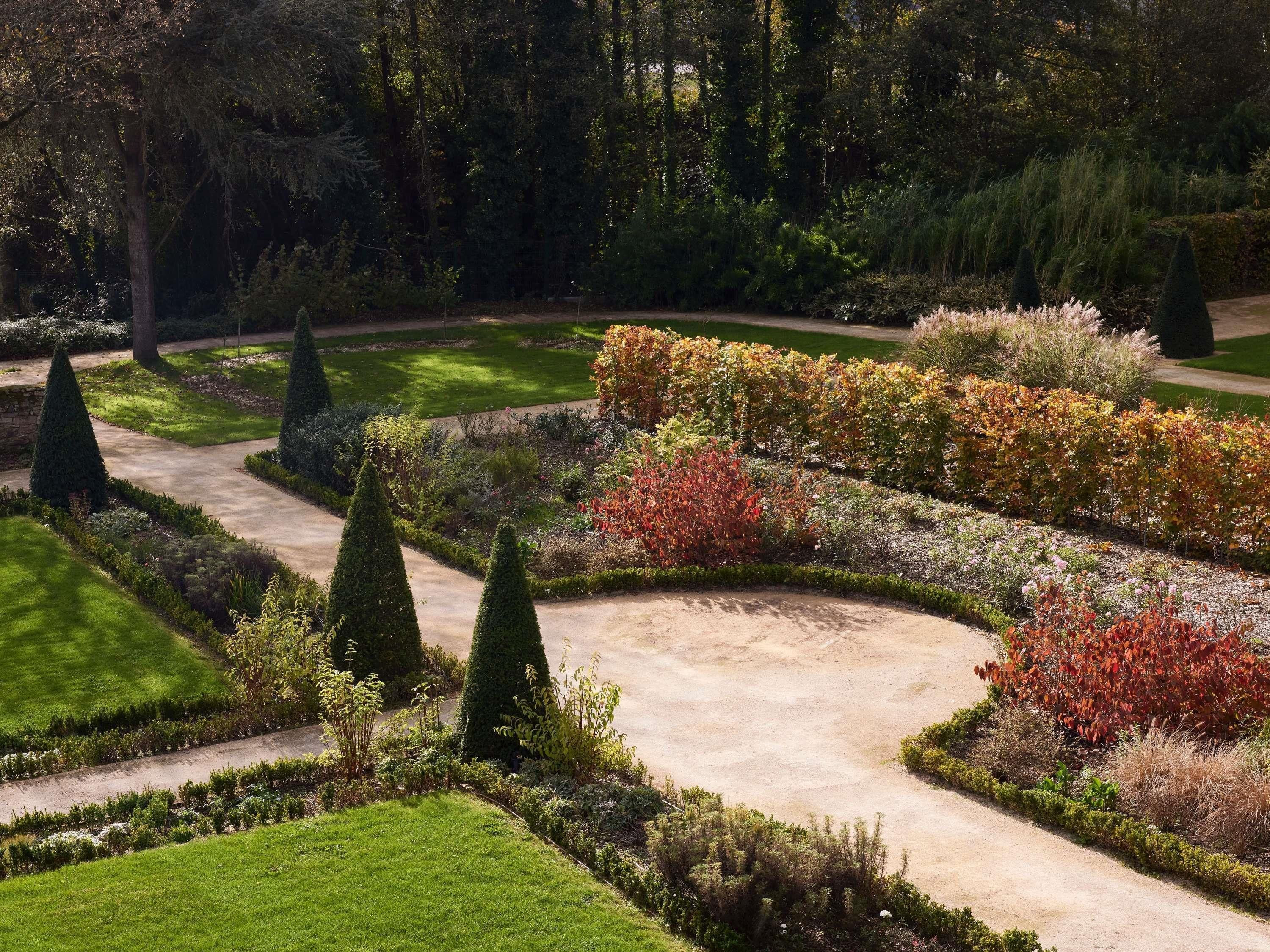 Een aangelegde tuin met een kronkelend pad, strak bijgesnoeide heggen en verschillende struiken en bomen.
