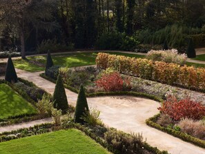Un jardin aménagé avec un sentier sinueux, des haies soigneusement taillées et une variété d’arbustes et d’arbres.