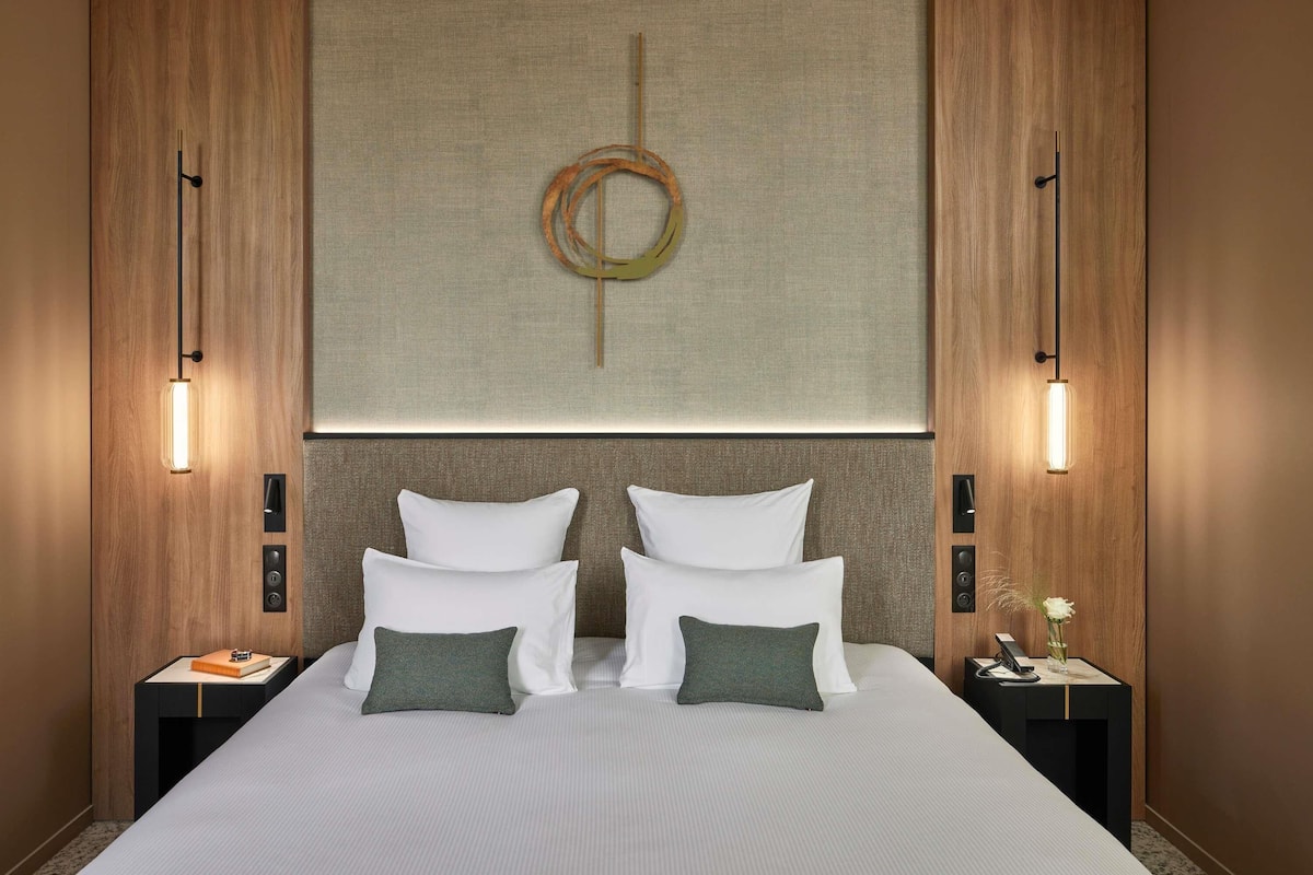 Ein Hotelzimmer mit einem großen Bett, zwei Nachttischen, einem an der Wand hängenden Kunstwerk und zwei Wandleuchten.