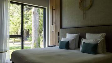 A large bed with white and green pillows, a wooden headboard, and a view of trees through a large window.