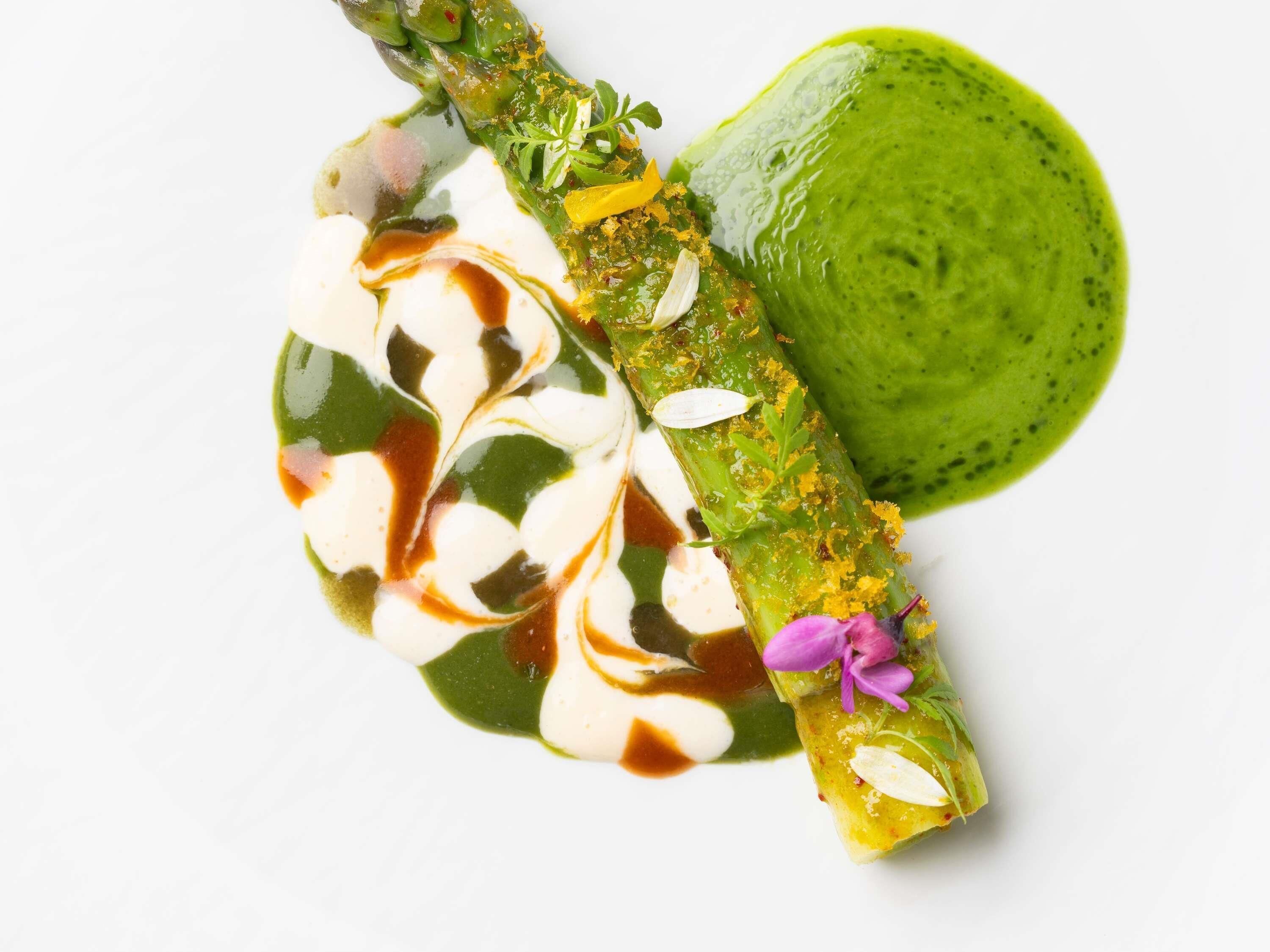 Un plat composé d’asperges, d’une sauce verte et d’une cuillerée de crème.
