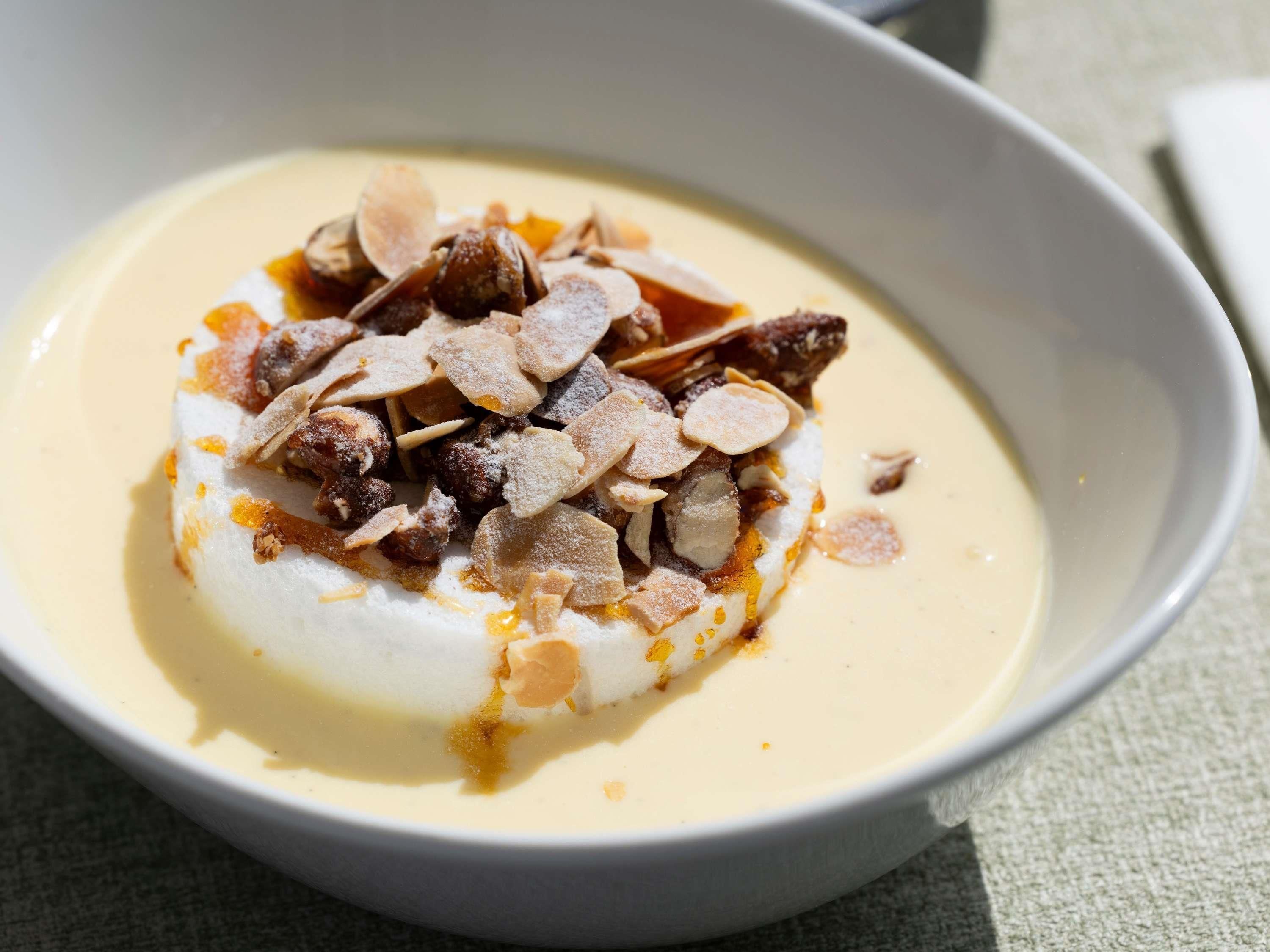 A bowl of dessert with a creamy base, topped with almonds and a caramel-like sauce.