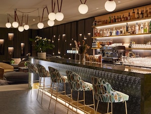 A bar area with a long counter, multiple stools, and a variety of bottles and glasses. - Domaine du Liziec Vannes - MGallery Collection (Vannes)