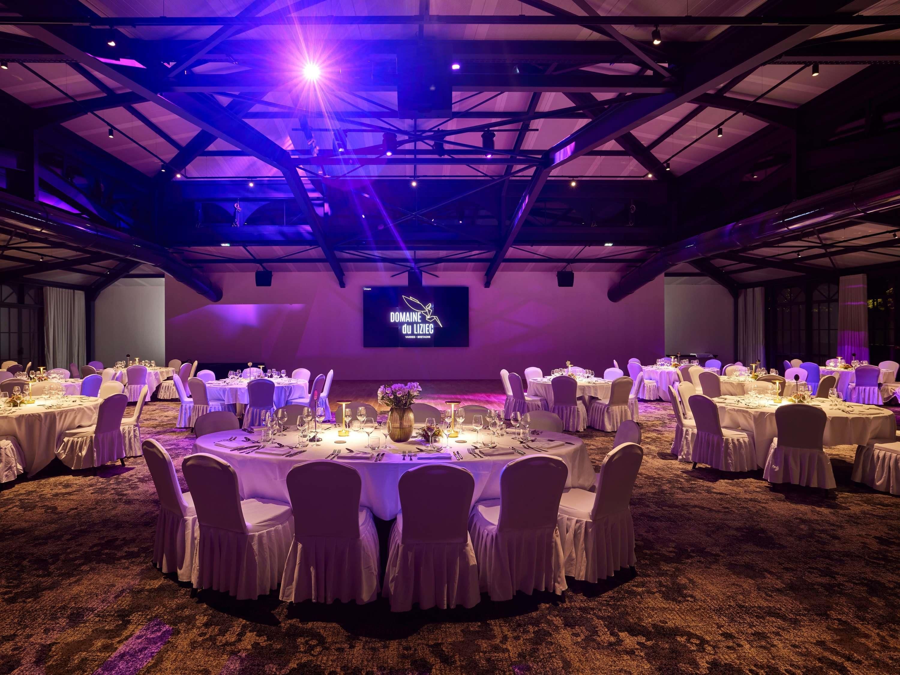 A banquet hall with round tables, chairs, and a stage with a screen.