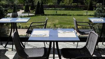 Buiten tafels met stoelen, uitzicht op een tuin en een pad van stenen.