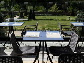 Tables et chaises installées à l’extérieur, avec vue sur le jardin et un chemin en pierre.