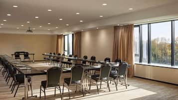 Un salón de conferencias con una larga mesa, sillas, un proyector y ventanas amplias con cortinas.