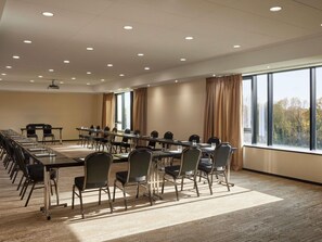 A conference room with a long table, chairs, a projector, and large windows with curtains.