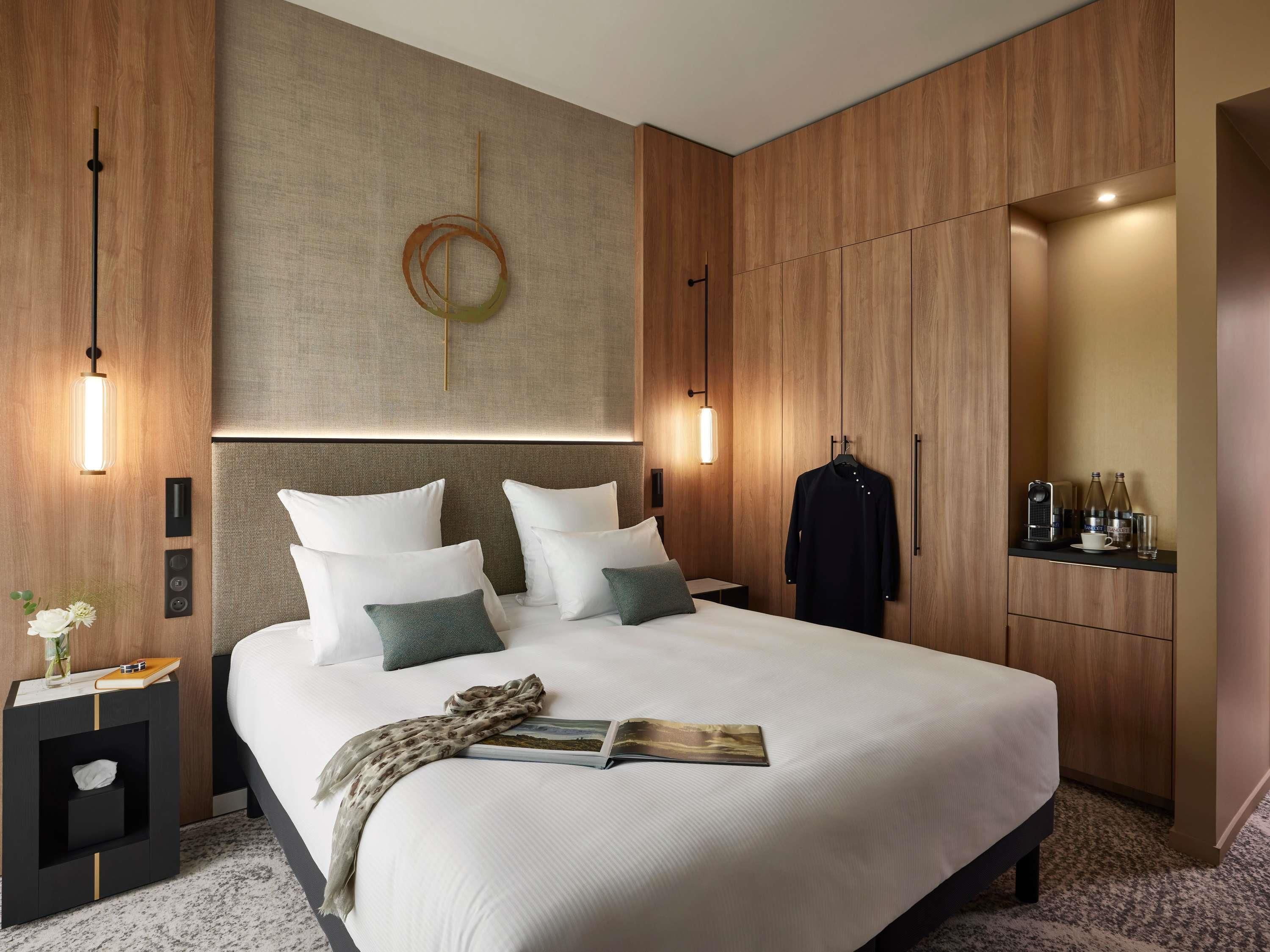 Una habitación de hotel moderna con una cama grande, una mesita de noche, un armario y un espejo.