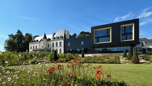 Un edificio moderno con una mezcla de arquitectura clásica y contemporánea, rodeado de un jardín bien cuidado con diversas plantas y flores.
