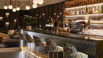 Zona de bar con una barra larga, varios taburetes y una gran variedad de botellas.