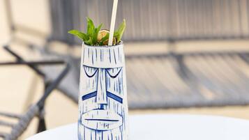 A tiki mug with a face design, a straw, and green leaves on a table.