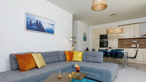 Un salon moderne avec un canapé d’angle gris, une petite table basse et un coin repas comprenant une table et des chaises en verre.