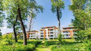 Un immeuble d’appartements moderne doté de nombreux balcons, entouré d’une végétation luxuriante et d’arbres.