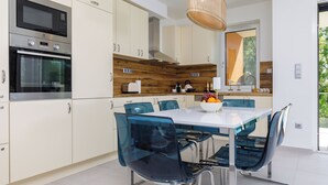 Une cuisine moderne avec des armoires blanches, un four encastré et un coin repas comprenant une table et des chaises en verre.