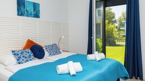 Une chambre d’hôtel avec un lit, une literie bleue, des coussins à motifs et une vue sur la verdure.