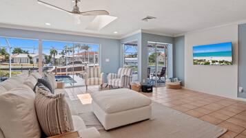 A spacious living room with a large window overlooking a pool area, a ceiling fan, and a mounted TV.