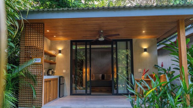 A modern house with a wooden deck, a sliding glass door leading to a bedroom, and a small kitchen area. - Serenity Wave Bungalow Beach & Jungle Escape + AC (Puerto Viejo de Talamanca)